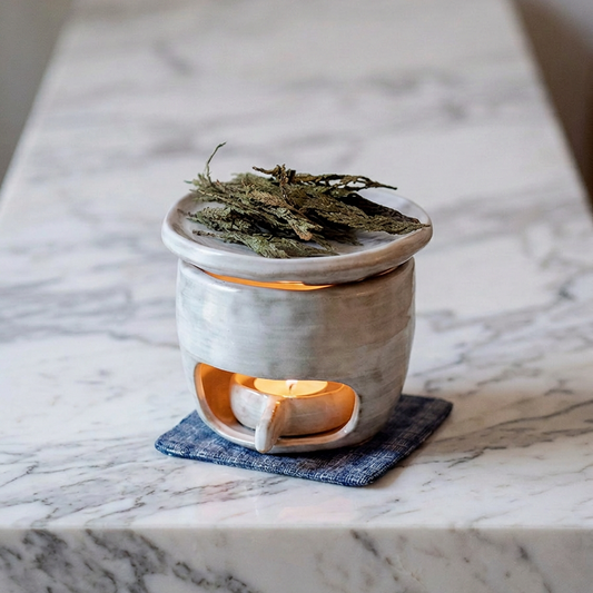 Rustic ceramic candle wax melts burner on a blue fabric coaster with burning tealight candle and dried botanical herbs on the top dish, marble counter setting - ShowerNest Australia