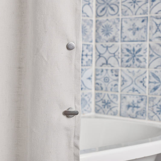 Shower curtain kept closed with a magnetic clip on patterned tiles