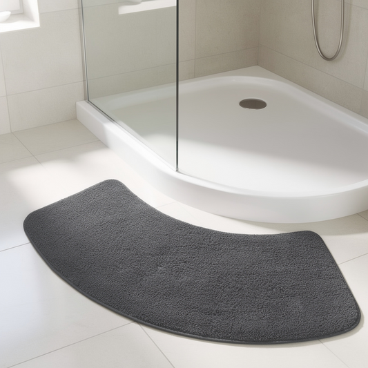 A dark gray curved bath mat placed on a white tiled floor in front of a white shower base with a glass door.