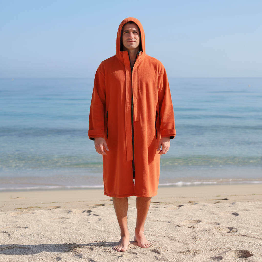 Man wearing an orange hooded surf changing robe on the beach – ShowerNest Australia
