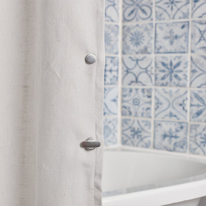 Shower curtain kept closed with a magnetic clip on patterned tiles