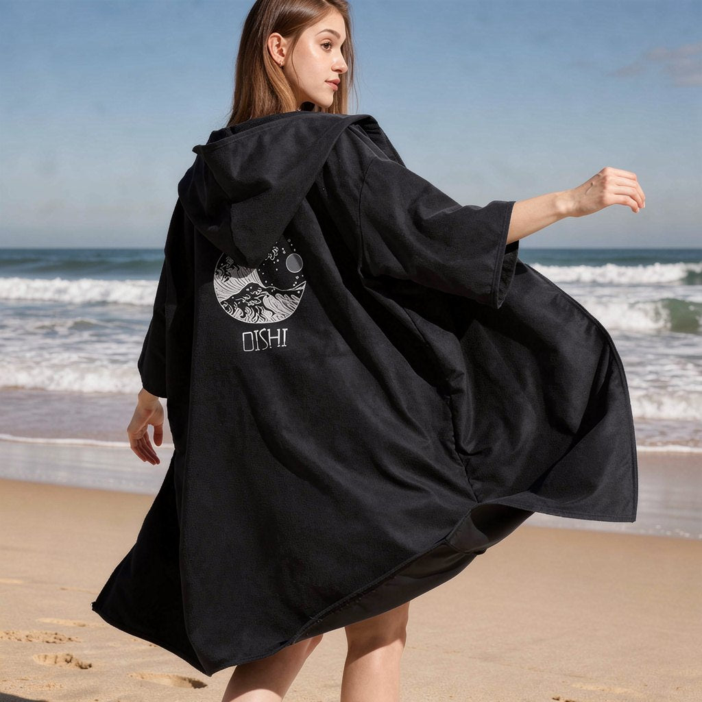 Woman wearing the black zip-up hooded changing robe on the beach, back view – ShowerNest Australia